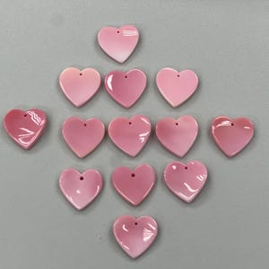 Puede incluir: Una colecci&oacute;n de 13 dijes de concha de coraz&oacute;n rosa con un agujero en la parte superior para encordar.