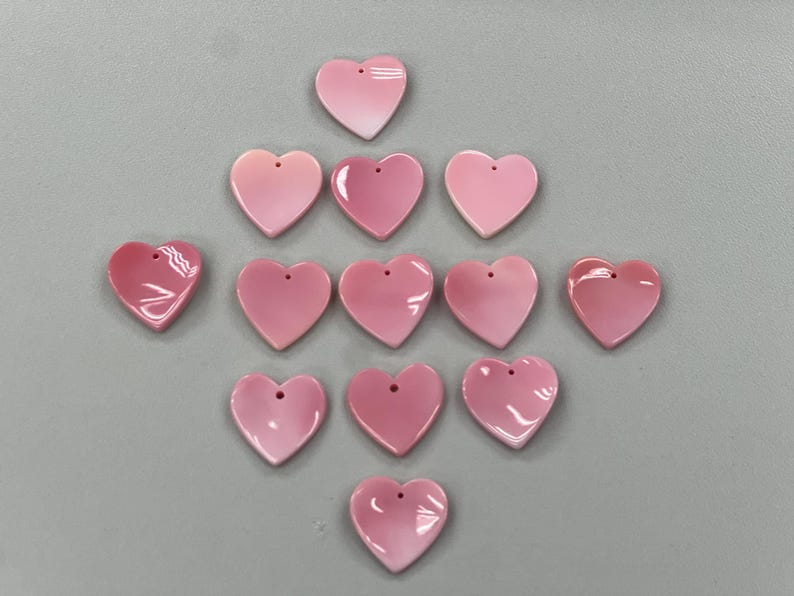 Puede incluir: Una colecci&oacute;n de 13 dijes de concha de coraz&oacute;n rosa con un agujero en la parte superior para encordar.