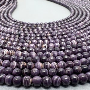 May include: A strand of round, purple and white striped beads. The beads are made of natural stone and have a polished finish.