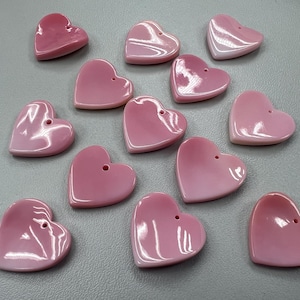 May include: A collection of 13 pink heart-shaped shell buttons. The buttons are all different sizes and have a smooth, polished finish.