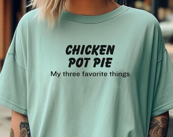 May include: A woman wearing a light blue t-shirt with the text "Chicken Pot Pie My three favorite things" in black. She is holding a to-go coffee cup.
