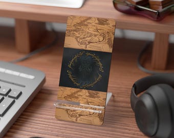 May include: A wooden phone stand featuring a map design with a black center panel. The center panel has a gold ring design with a tree in the middle. The stand is on a wooden desk.