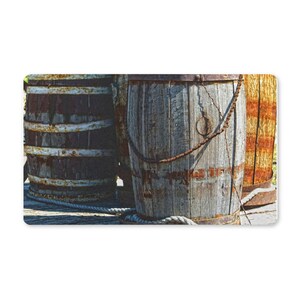 May include: Three weathered wooden barrels with rusty metal bands and a rope. The barrels are various shades of brown and gray, suggesting age and exposure to the elements. A chain hangs from one barrel.