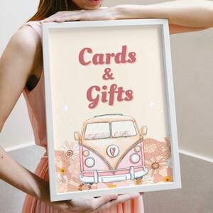 Puede incluir: Un marco blanco con un fondo amarillo claro y el texto "Cards & Gifts" en rosa. Una furgoneta vintage rosa y amarilla con un corazón en la parte delantera está rodeada de flores rosas y amarillas.