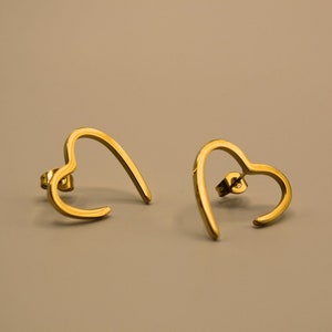 Könnte beinhalten: Ein Paar goldene Ohrringe in Herzform. Die Ohrringe sind aus dünnem Metall und haben ein schlichtes Design.
