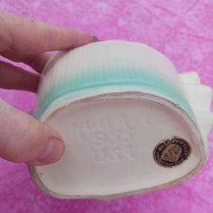 May include: A vintage Hull Pottery vase, featuring a white base with a turquoise and white top. The bottom of the vase is stamped with "Hull 1935 USA" and a gold foil label. The vase has a ribbed design.