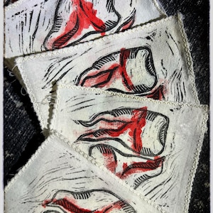 May include: A stack of white fabric squares with a repeating abstract design in black and red. The edges of the squares are finished with a decorative stitch. The overall aesthetic is reminiscent of a linocut print.