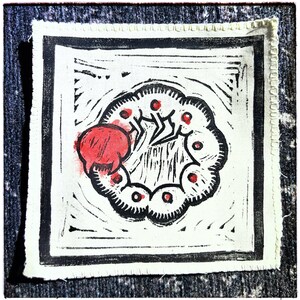 May include: Square, off-white fabric patch with a black border and a hand-carved design. The design features a red, rounded shape on the left and a black, insect-like figure inside a circular pattern with red dots.
