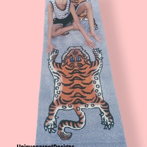 May include: A long, gray rug with a tiger design. The rug features three tigers, two smaller tigers at the top and one larger tiger at the bottom. The rug is on a pink background.