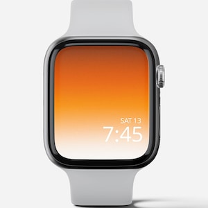 Puede incluir: Un Apple Watch plateado con una banda deportiva blanca. La esfera del reloj es un degradado de naranja y blanco con la hora mostrada como 7:45 y la fecha como SÁB 13.