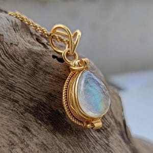 May include: A gold-colored necklace with a teardrop-shaped pendant. The pendant features a pearlescent, iridescent stone set in a detailed gold frame. The chain is delicate and the pendant is suspended from a decorative bail.