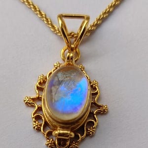 May include: Gold-toned pendant necklace featuring an oval, iridescent gemstone. The gemstone is set in a decorative, filigree-style frame. The necklace chain is a twisted rope design. The pendant is approximately 1.5 inches long.