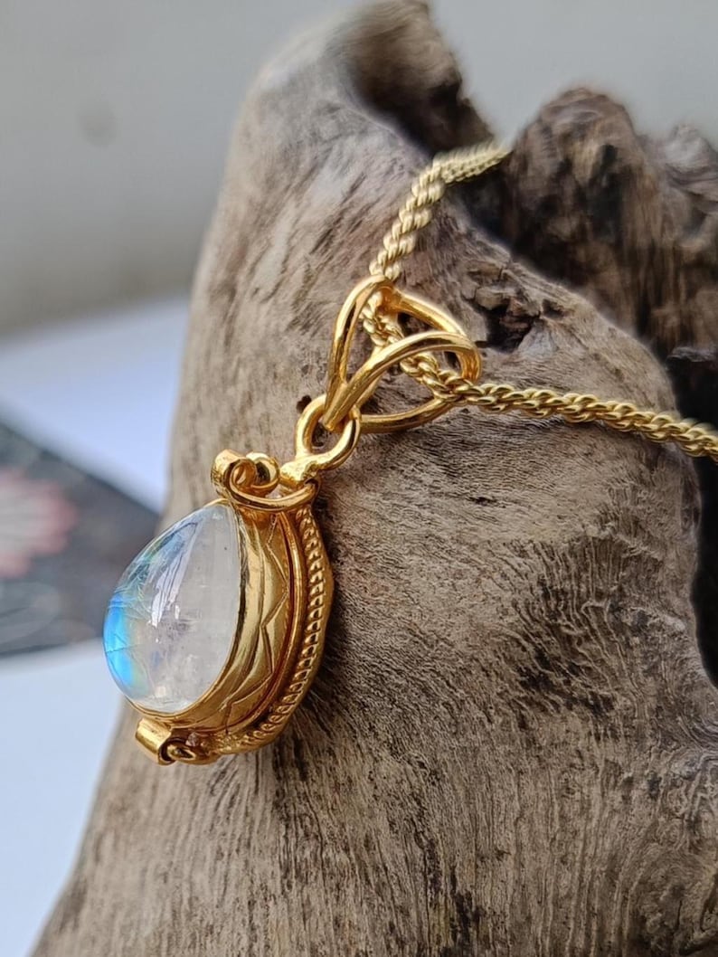 May include: A gold-colored pendant necklace featuring a pear-shaped, iridescent moonstone. The moonstone is set in a detailed, ornate gold bezel. The chain is a delicate, woven design.