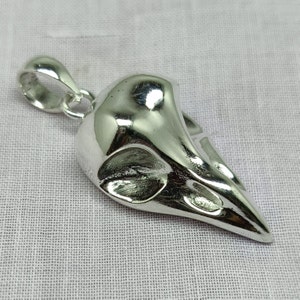 Puede incluir: Un colgante de plata con forma de cr&aacute;neo de p&aacute;jaro. El colgante tiene un bucle en la parte superior para sujetarlo a una cadena.