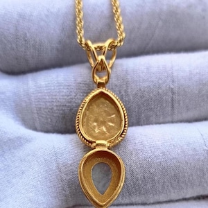 May include: A gold-colored locket necklace with a teardrop-shaped pendant. The pendant opens to reveal a small compartment. The necklace chain is a twisted rope design. The locket has a decorative rope-like border.