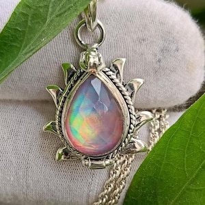 Op de afbeelding: Een zilveren hangerketting met een druppelvormige, iriserende edelsteen. De edelsteen is gezet in een decoratief zilveren frame met een zonnesterontwerp. De ketting heeft een fijne zilveren ketting.