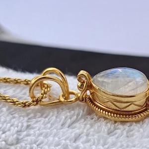 May include: A gold-colored necklace with a pendant featuring a pear-shaped, iridescent gemstone. The pendant is set in a detailed gold bezel with decorative elements. The chain is a delicate, twisted rope design.