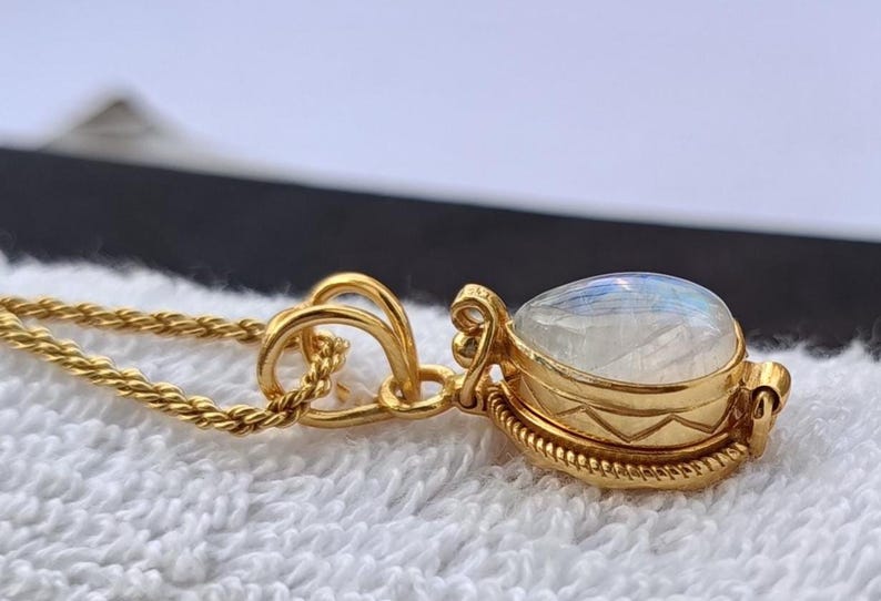May include: A gold-colored necklace with a pendant featuring a pear-shaped, iridescent gemstone. The pendant is set in a detailed gold bezel with decorative elements. The chain is a delicate, twisted rope design.