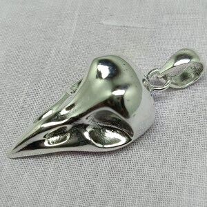 Puede incluir: Un colgante de plata con forma de cr&aacute;neo de p&aacute;jaro con un bucle para sujetar una cadena.