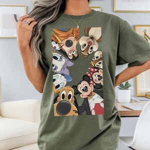 May include: An olive green t-shirt with a graphic of Disney cartoon characters, including Mickey and Minnie Mouse, Goofy, Donald Duck, and Chip and Dale. The shirt is made of a soft material.