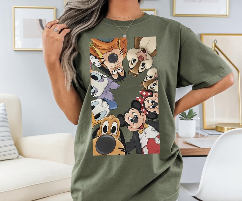May include: An olive green t-shirt with a graphic of Disney cartoon characters, including Mickey and Minnie Mouse, Goofy, Donald Duck, and Chip and Dale. The shirt is made of a soft material.
