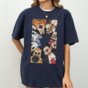 May include: Dark navy blue t-shirt with a rectangular graphic showcasing cartoon characters like Mickey and Minnie Mouse. The characters are arranged in a circle. The t-shirt has a relaxed, oversized fit.
