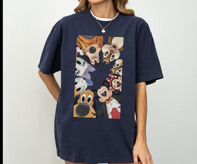 May include: Dark navy blue t-shirt with a rectangular graphic showcasing cartoon characters like Mickey and Minnie Mouse. The characters are arranged in a circle. The t-shirt has a relaxed, oversized fit.