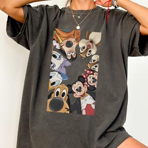 May include: Dark grey oversized t-shirt with a colourful graphic of Disney cartoon characters, including Mickey Mouse, Minnie Mouse, and Pluto. The design is centred on the front of the shirt. The shirt has short sleeves and a relaxed fit.