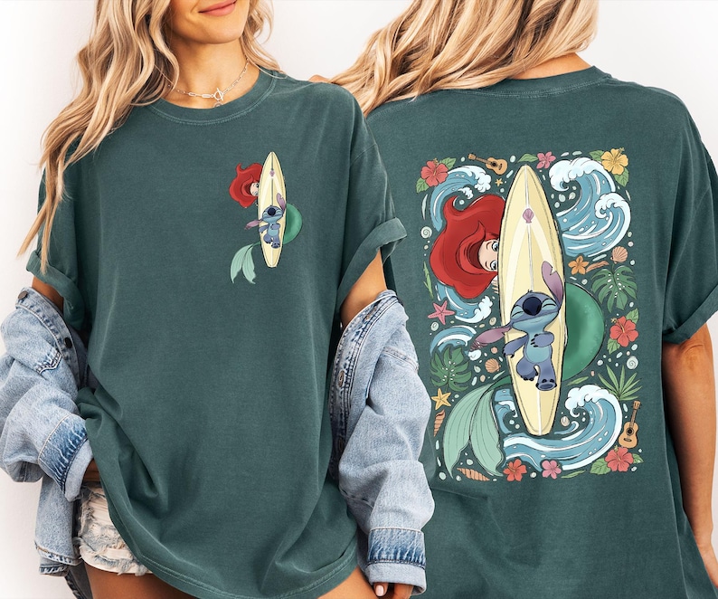 May include: Dark teal t-shirt featuring a cartoon design of Ariel and Stitch surfing on a surfboard. The front has a small graphic, while the back showcases a larger, detailed illustration with waves, flowers, and tropical elements.