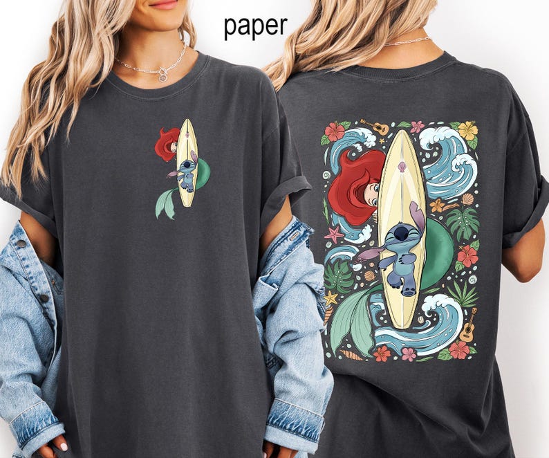 May include: Dark gray t-shirt featuring a cartoon design of Ariel and Stitch surfing. The front has a small image of Ariel and Stitch on a surfboard. The back has a larger image with waves, flowers, and tropical leaves.