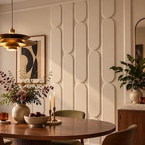 Op de afbeelding: Een ronde houten eettafel met een gecanneleerde voet, omringd door vier houten stoelen met olijfgroene gestoffeerde zittingen. Op de tafel staan een keramische vaas met bloemen, een schaal met fruit en twee hoge kaarsen in koperen houders.