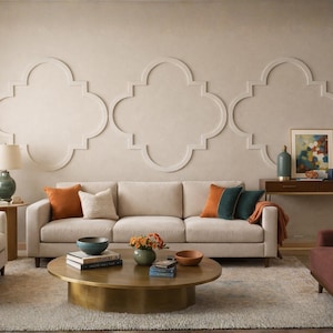 May include: A beige three-cushion sofa with orange and teal throw pillows, a round brass coffee table, a green ceramic table lamp, a dark wood console table, and a maroon armchair, set against a wall with three large white quatrefoil mouldings.