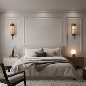 May include: A bedroom scene featuring a bed with neutral-toned bedding, a dark gray throw blanket, and decorative pillows. Two wooden bedside tables flank the bed, each with a lamp. Two wall sconces with a warm glow are mounted on the wall.