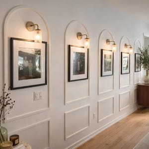 Decorative wall with arched wall molding, framed landscape pictures, wall sconces, and a wooden console table.