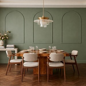 May include: A dining room featuring a square wooden table with four upholstered chairs, set against a sage green wall with three arched moldings. A tiered brass and glass pendant light hangs above, while a console table holds a floral arrangement.