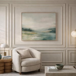 Op de afbeelding: Een serene woonkamer met een landschapsschilderij in een houten lijst boven een cr&egrave;mekleurige, afgeronde fauteuil. Een moderne vloerlamp met twee bolvormige lampen en een kleine bijzettafel met een lamp en decoratieve items maken de ruimte compleet.