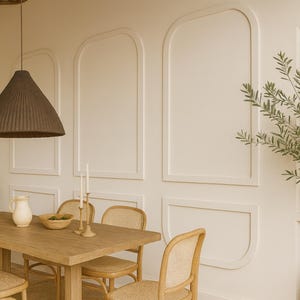 Könnte beinhalten: Ein Esszimmer mit einem rechteckigen Holztisch und vier Stühlen mit Sitzflächen und Rückenlehnen aus geflochtenem Rohrgeflecht. Eine dunkelbraune, konische Pendelleuchte hängt über dem Tisch. Die Wand zeigt bogenförmige Zierleisten und ein Regal.