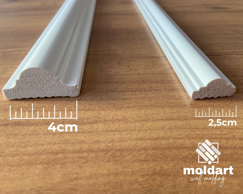 May include: Two white decorative molding pieces. One is 4 cm wide, the other is 2.5 cm wide. The molding has a curved, decorative edge. The background is a wooden surface. The logo "moldart wall molding" is in the bottom right corner.