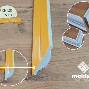 Op de afbeelding: Witte zelfklevende wandlijst met een decoratief profiel. De afbeelding toont een close-up van de lijst waarbij de zelfklevende achterkant wordt verwijderd. De tekst "PEEL & STICK Available" is zichtbaar.