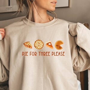 May include: Sand-coloured sweatshirt with the text "DIE FOR THREE PLEASE" in red. The design features watercolour illustrations of four different pie slices. The sweatshirt is a relaxed fit.