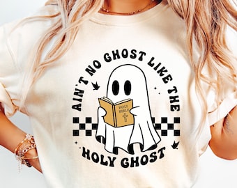 Op de afbeelding: Een wit T-shirt met een zwart-witte afbeelding van een geest die een boek vasthoudt met de tekst "Holy Bible". De tekst op het shirt luidt "Ain't no ghost like the Holy Ghost".