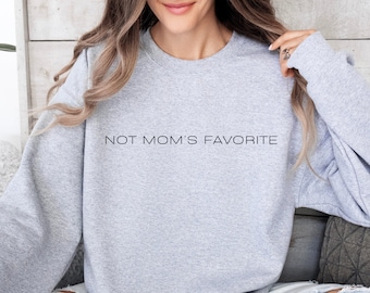 May include: A light gray sweatshirt with the text "NOT MOM'S FAVORITE" in black. The sweatshirt is a crew neck style and appears to be made of a soft material. The image shows the sweatshirt on a person.