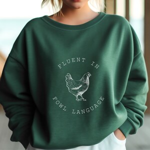 May include: A green sweatshirt with a white graphic of a chicken and the text "Fluent in Fowl Language".