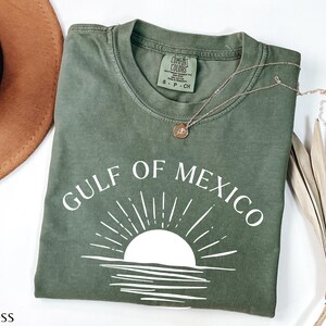 May include: A green t-shirt with a white graphic of a sunset over water and the text "GULF OF MEXICO".