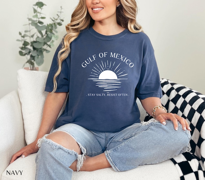 May include: A navy blue t-shirt with a white graphic of a sunset over water and the text "Gulf of Mexico. Stay Salty, Resist Often."