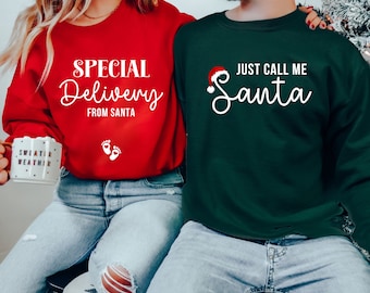 May include: Red and dark green Christmas sweatshirts. The red sweatshirt says "SPECIAL Delivery FROM SANTA" with baby footprints. The dark green sweatshirt says "JUST CALL ME Santa" with a Santa hat.