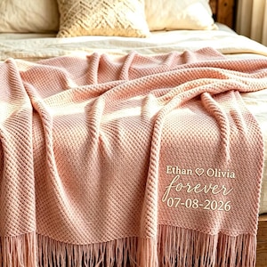 May include: A soft, light pink knitted throw blanket with a textured pattern and fringe trim. The blanket features white embroidered text that reads Ethan ♡ Olivia, forever, and the date 07-08-2026, centred on the lower right corner.