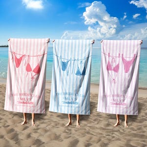 Puede incluir: Tres toallas de playa a rayas verticales en rosa, azul y lavanda, cada una con un diseño de bikini y el texto "THE BRIDE CLUB EMILY'S Bachelorette CAPE COD AUG 2005". Las toallas se sostienen en una playa de arena.