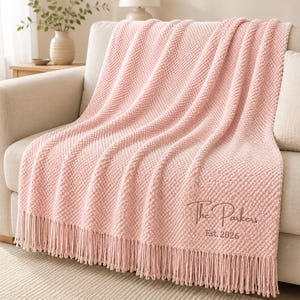 May include: A soft, light pink textured throw blanket with a waffle-knit pattern and long fringe along the bottom edge. The blanket features custom embroidery in a dark thread that reads The Parkers and Est. 2026 in a cursive and print font.