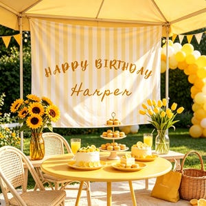 Könnte beinhalten: Ein gelb-weiß gestreifter Geburtstagshintergrund mit dem Text HAPPY BIRTHDAY Harper, ein Tisch mit Kuchen, Macarons, Sonnenblumen in einer Glasvase und gelben Tulpen in einer Glasvase, unter einem gelben Vordach mit einem Ballonbogen.